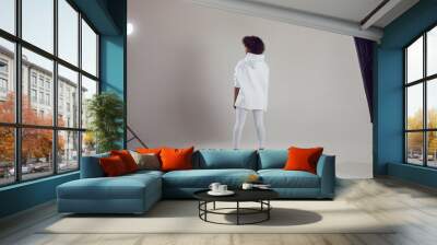 African American woman with puffy hair in a white hoodie and leggings stands on a white background in a photo studio. Wall mural