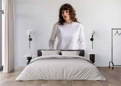 Young woman with curly hair in a white long sleeve t-shirt stands on a white background. Mock-up. Wall mural