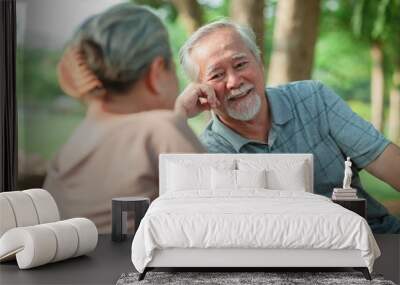 A man and woman are sitting in a park, smiling and laughing. The man is wearing a gray shirt and the woman is wearing a brown shirt. They seem to be enjoying each other's company Wall mural