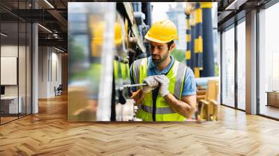 A man in a yellow and green vest is working on a machine. He is wearing a hard hat and gloves Wall mural