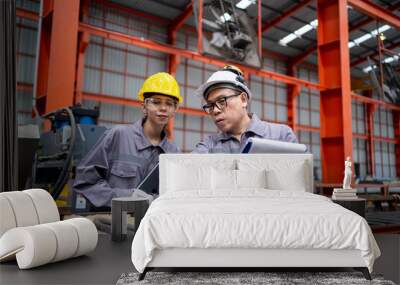 Two workers in orange and grey clothing are looking at a piece of machinery. One of them is holding a clipboard Wall mural