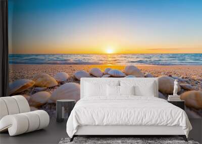 A beautiful sunset over the ocean, with a collection of seashells scattered on the sandy beach, creating a peaceful scene. Wall mural