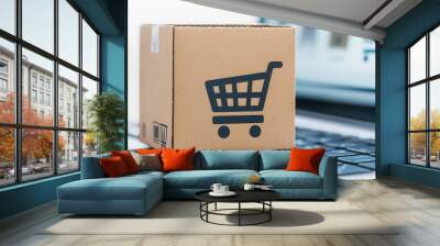 A cardboard box with a shopping cart icon sits on a laptop keyboard, symbolizing online shopping and e-commerce. Wall mural