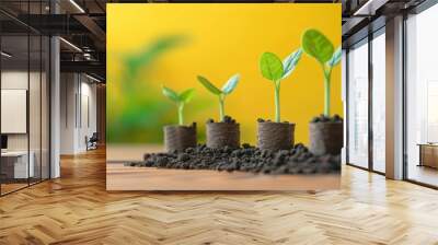 Four small plants growing in soil, representing growth and development, with a yellow background and blurred green leaves. Wall mural