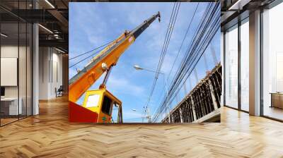 Mobile cranes at construction sites. A large yellow truck mounted crane sits beside a building under construction and has low voltage lines on a cloudy sky background. Selective focus Wall mural