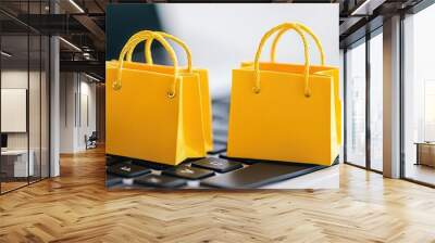 Two yellow shopping bags are placed on a laptop keyboard, symbolizing online shopping and e-commerce. Wall mural