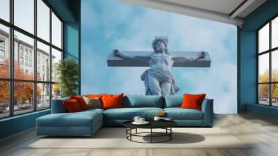 A white marble statue of Jesus Christ on the cross against a cloudy blue sky. Wall mural