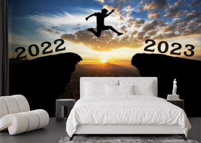 A young man jump between 2022 and 2023 years over the sun and through on the gap of hill  silhouette evening colorful sky. happy new year 2022. Wall mural