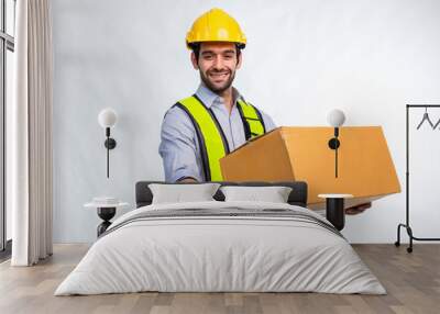 Delivery man employee in yellow hard hat hold cardboard box isolated on white background. Delivery man holding cardboard boxes. Smiling delivery man standing on white background Wall mural