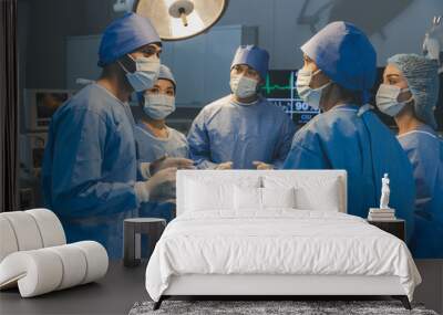 Surgeons team working with Monitoring of patient in surgical operating room. The doctors and nurses brainstorm power assisted surgery. A team of professional doctors perform surgery in a hospital Wall mural