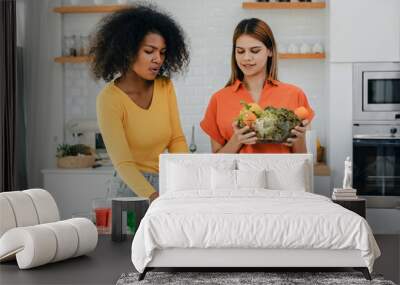 Two women choosing between vegetable and sausage, organic food vs gmo products. Young woman making choice to eat healthy food in kitchen for her comparing junk fatty unhealthy meal Wall mural