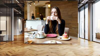 Young woman drinks tea in a cafe and enjoys a delicious dessert Wall mural