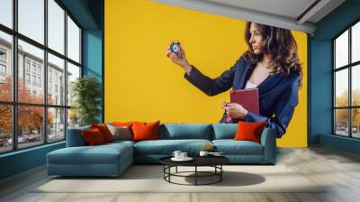 The European woman dressed elegantly as a teacher or business lady, holds a watch in her hand and holds a notebook in her hand, feels well placed, with a smile on her face and energetic Wall mural