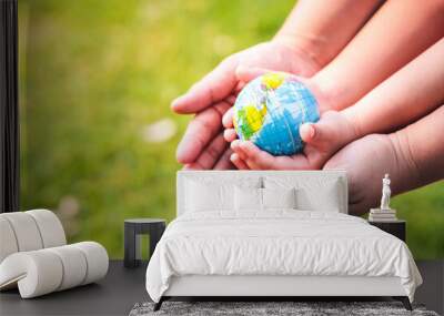 World environment day concept.  A mother's hand embrace her little daughter's hands. Child hand's who is holding carry the world. Blurred green lawn background. Protect our globe. Copy space. Wall mural