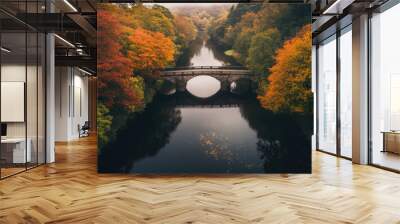 Bird eye view of a historic stone bridge crossing a calm river surrounded by autumn foliage, vibrant red and gold leaves reflecting on the water. Wall mural