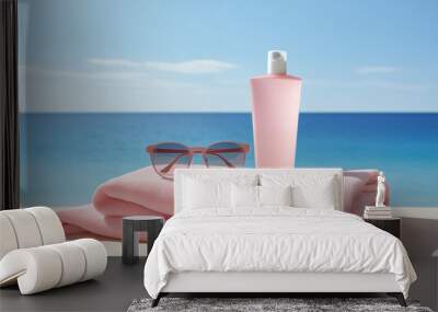 A bottle of sunscreen sits on a towel next to a pair of sunglasses. The scene is set on a beach, with the ocean in the background. Concept of relaxation and leisure Wall mural