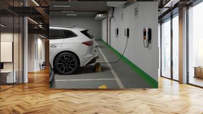 Generic electric crossover car connected to charging box. EV vehicle plugged in energy station, recharge battery at shopping mall or urban city house parking lot. Wall mural