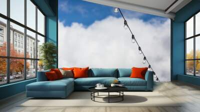 Lamp string hanging outside against a cloudy blue sky background Wall mural