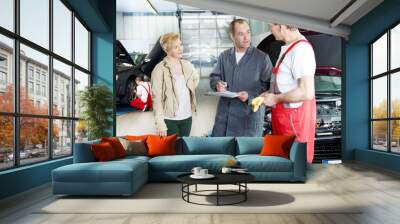 Female customer takes advise by motor mechanics in a garage Wall mural