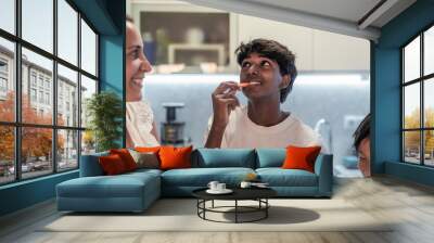 a boy of indian origin tastes a vegetable in the kitchen while his mother and brother accompany him. family cooking concept. healthy and natural food. Wall mural