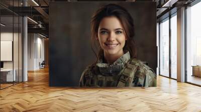 Cheerful female soldier smiling at the camera while standing against a studio background. Brave young servicewoman wearing the camouflage military uniform of the United States Armed Forces Wall mural