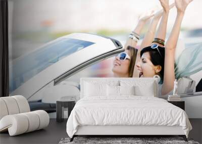 Female friends driving cabriolet with the hands up Wall mural