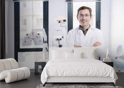 Portrait of handsome eye doctor sitting with ophthalmologic device in the cabinet Wall mural