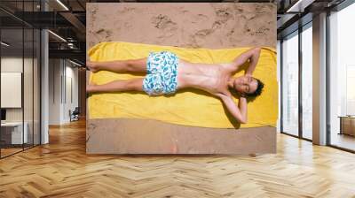 Teenage boy lying on the towel on a fabulous day at the beach. Wall mural