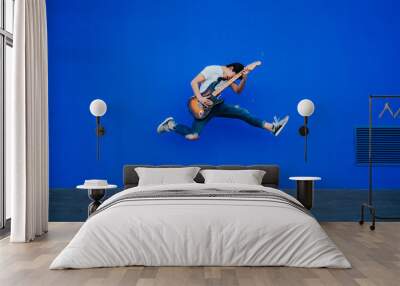 young man jumping with electric guitar on blue background Wall mural