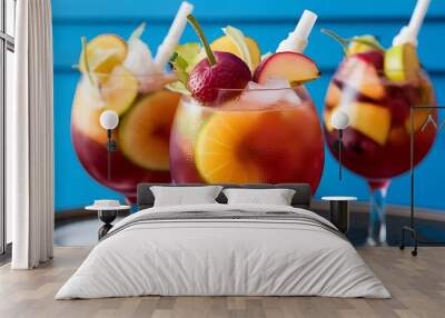 A closeup of delicious iced fruit cocktails with straws on the table against a blue background Wall mural