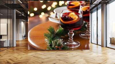 Close up view of mulled wine in glasses with orange pieces and spices on wooden surface with bokeh lights on backdrop Wall mural