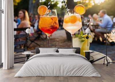 Two glasses with different summer refreshing cocktails on the table of a summer cafe in the park. Aperol syringe and lemonades. Wall mural