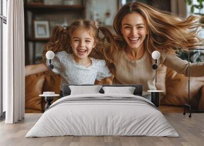 A woman and a little girl are playing together on a couch Wall mural