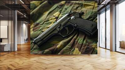 A black handgun is lying on a green camouflage fabric Wall mural