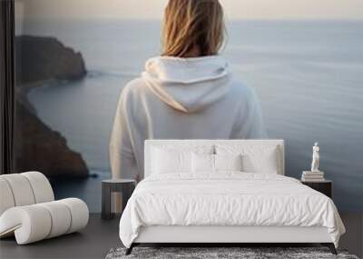 This mockup features a female model in a blank white hoodie, meditating on a cliff overlooking a calm ocean view at dawn. Wall mural