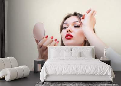  Charming  woman with big red lips in white blouse applying magnetic fake eyelashes isolated on beige color. Beauty treatment concept for cosmetologist. Pure perfect skin. Selective focus. Copy space Wall mural