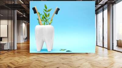 Bamboo wooden toothbrushes with green branch leaves in white toothbrush holder in form of tooth on blue pastel background. Dental health medical care concept. Copy space. Eco friendly goods Wall mural