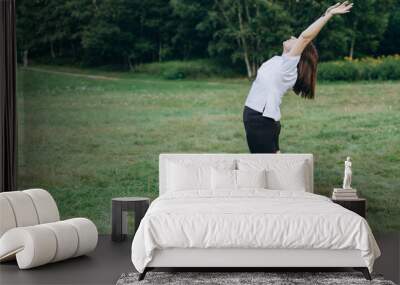 Young Woman Is Practicing Yoga In A Park, Standing On A Mat With Her Arms Raised In A Forward Bend Pose. Back Bend Asana Wall mural