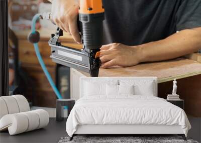 carpenter using nail gun or brad nailer tool on wood box in a workshop ,furniture restoration woodworking concept. selective focus. Wall mural