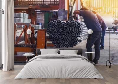 Two workers in uniform using lifting machines to move metal pipe in a sheet metal factory. Wall mural