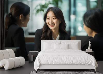 A Japanese business woman is talking to two other women in the office,one of them holding documents and smiling at each other. Wall mural