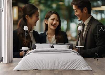 A Japanese business woman is talking to two other women in the office,one of them holding documents and smiling at each other. Wall mural