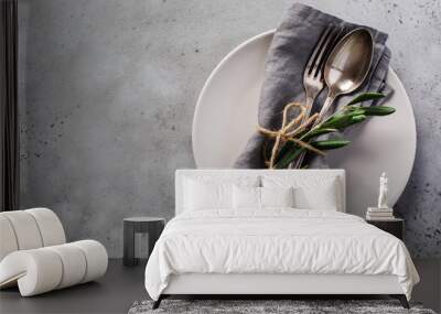 Rustic vintage set of cutlery. Plate with grey linen napkin, fork and spoon, olive tree branch over rustic concrete gray old background. Fall holiday table decoration setting. Top view, copy space. Wall mural