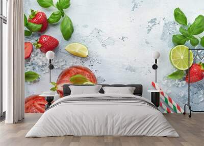 Two glasses of punch and fresh ingredients for making lemonade, infused detox water or cocktail. Strawberries, lime, mint, basil, ice cubes and shaker on grey stone or concrete background. Top view. Wall mural