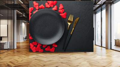 Valentines day romantic table setting. Empty or closeup of a dinner black plate, knife, fork and decorative silk hearts on black background. Holiday concept. Copy space for inscriptions. Wall mural