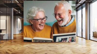 A joyful elderly couple sharing laughter while looking through a photo album at home, showcasing love and cherished memories. Wall mural