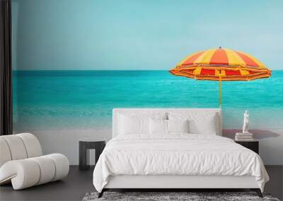 Colorful beach umbrella on a serene sandy shore with turquoise water. Wall mural