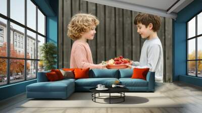 Two children sharing a plate of fresh strawberries outdoors. Wall mural