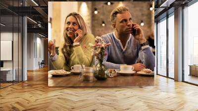 Couple sitting in cafe and talking on mobile phones Wall mural