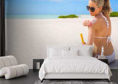 Woman sunbathing on the beach and applying sunscreen Wall mural